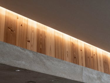 Detalle arquitectónico de un foseado de iluminación en techo de concreto, transición limpia hacia un panel de madera noble de roble, luz cálida difusa.