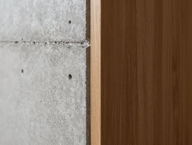 Extreme close-up of a flawless concrete wall transitioning to a warm oak wood joint, architectural precision, soft side lighting highlighting textures.