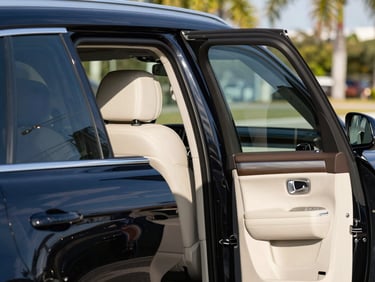 A clean luxury SUV passenger door held open, bright Florida sunshine reflecting on the polished black paint.