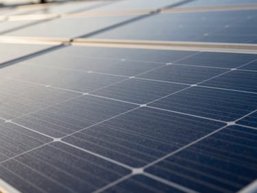 Macro shot of a solar panel surface reflecting blue sky, with a subtle grid pattern visible, industrial editorial photography, crisp daylight, cool blue and amber tones, sharp focus, technical detail, 35mm lens