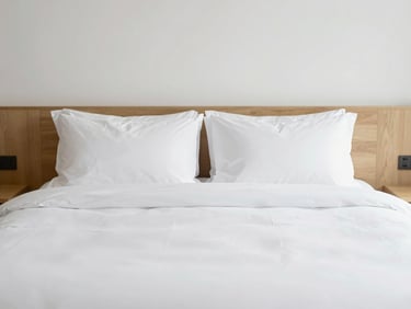 Minimalist hotel room bedding, clean white sheets, natural wood accents, bright diffused light
