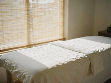 Soft shadows on a clean linen-draped massage table, warm afternoon light filtering through bamboo blinds, minimalist serene studio setting, 35mm editorial.