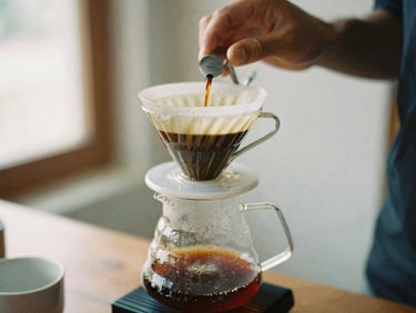 Close-up of a V60 pour-over coffee dripping into a glass carafe, barista's hands carefully pouring water, soft side-lit window daylight, rich espresso and cream tones, shallow depth of field, 35mm film