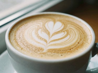 Close-up of a flat white with latte art in a ceramic mug, soft side-lit window daylight, rich espresso and cream tones, shallow depth of field, 35mm film