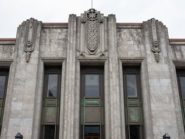 Straight-on shot of an art deco facade with stone carvings and bronze details, clean overcast lighting, CDMX