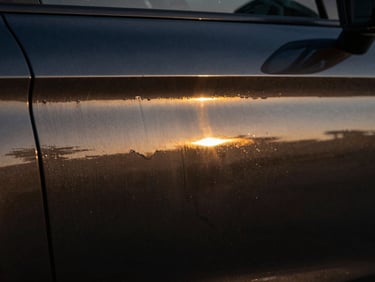 Macro shot of a dark car panel, showing a subtle layering effect of wax, liquid reflection, warm gold accents, studio light