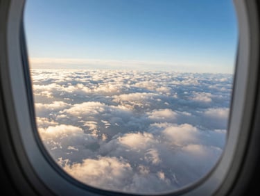 Clean aircraft window overlooking a vast expanse of clouds during golden hour, first-person perspective, wide-angle cinematic lens, rich saturated blues and whites.