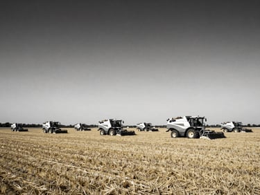 Wide environmental landscape of a modern farm with large-scale agricultural machinery operating under dramatic natural daylight