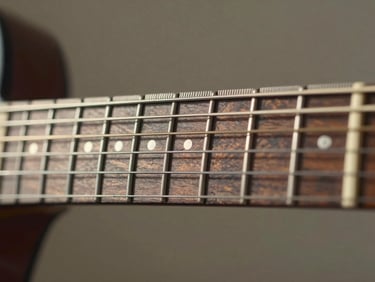 Close-up of a guitar fretboard under bright north-facing daylight, frets clearly visible, ruler measuring fret height, neutral background, no faces