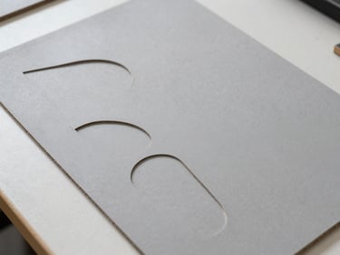 Overhead shot of a laser-cut thick leather template next to a piece of dense grey cardboard on a clean workbench