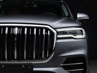 Close-up of a polished chrome front grille of a premium SUV, dramatic low-key studio lighting, deep metallic reflections.
