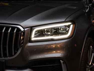 Dramatic close-up of a polished chrome grille and LED headlight of a luxury SUV, low-key studio lighting, gold reflections