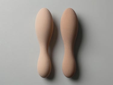 Top-down studio photograph of two masturbator sleeves placed side by side on a neutral grey-white surface, overhead hard light revealing material detail and form factor, clean background, no people, no implied use