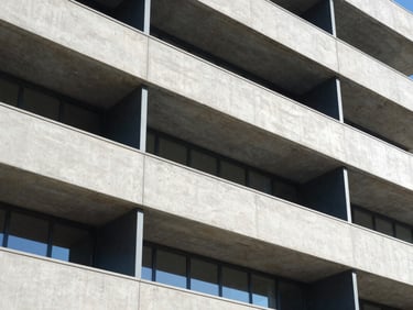 Sharp architectural drawing overlaid on a modern concrete and steel building facade, bright daylight, high contrast shadows