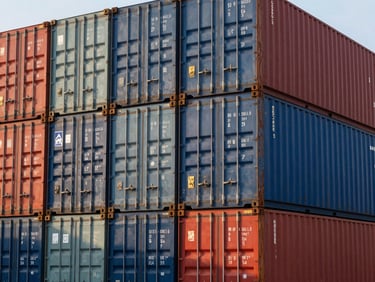Close-up of stacked blue and red shipping containers at a busy port terminal during golden hour, realistic industrial lighting.