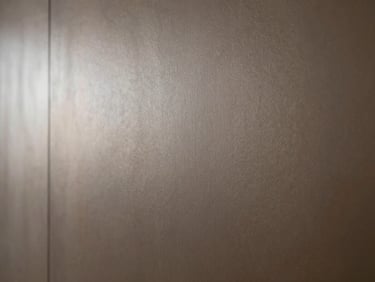 Extreme macro detail of hand-applied bronze metallic wall finish, catching soft directional daylight