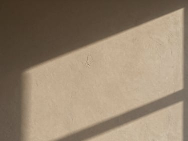 Close-up of coarse troweled plaster finish, deep shadows from low-angle warm daylight