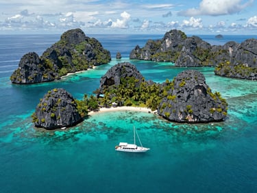 Aerial view of iconic limestone karst islands of Raja Ampat, crystal clear turquoise water, a small luxury yacht anchored