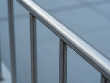 Sharp industrial photograph of a minimalist stainless steel handrail on a concrete staircase, cold reflections, macro detail