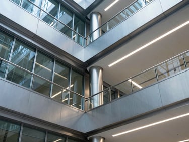 Architectural general shot of a modern office building atrium, extensive stainless steel balustrades, clean glass integration, cold high-contrast lighting.