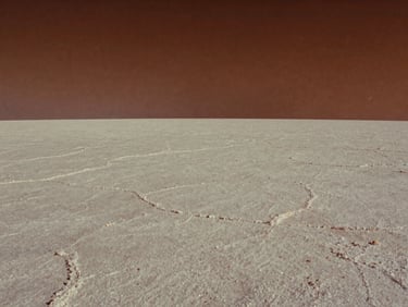 Cinematic film still, extreme wide shot of a vast white salt flat under a burning midday sun, minimalist composition.