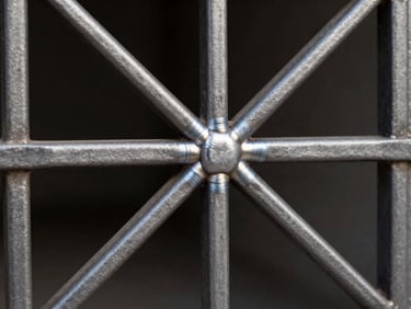 Tight detail shot of a custom steel window grill with a geometric pattern, studio strobe lighting revealing weld seams and surface finish, sharp focus on the intersecting steel bars and powder-coated texture