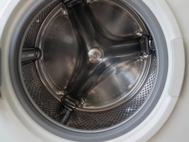 Close-up of a modern stainless steel washing machine drum interior, clean metallic reflections, sharp focus on the drum pattern, bright daylight