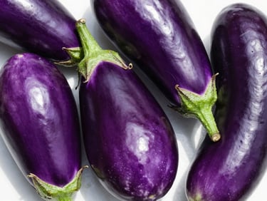Vivid glossy purple brinjal (eggplant) specimens on a white surface, natural daylight from above, showing smooth unblemished skin and fresh green calyx, true colour, extreme close-up