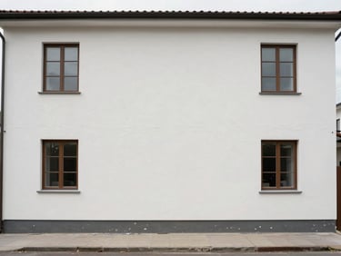 Residential building facade after cleaning, overcast daylight showing uniform clean plaster surface and tidy ground-level area, before-cleaning grime line barely visible at base