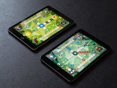 Overhead flatlay of two Android tablets showing a strategy game board, cool overcast lighting, dark desk surface, clean UI visible on screens