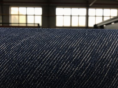 High-contrast macro shot of a woven denim fabric texture, showing intricate weave pattern, dramatic factory light.