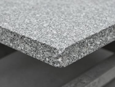 Extreme close-up of a freshly planed grey granite slab, showing sharp cut edges and crystalline mineral structure under cold overcast daylight, desaturated slate tones.