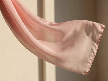 A soft pink chiffon scarf fluttering gently in a warm breeze, captured in close-up showing the fine weave and delicate texture, outdoor natural light.