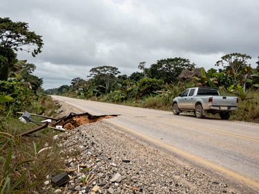 Wide shot of a collapsed section of a rural road in the Amazonas highlands, gravel and mud exposed, a local pickup truck stopped at the edge, flat grey overcast sky above