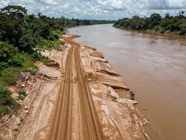 Overhead view of a river bank in the Amazonian lowlands where machinery tracks cut through exposed clay soil, wide environmental framing, overcast natural daylight, no people visible