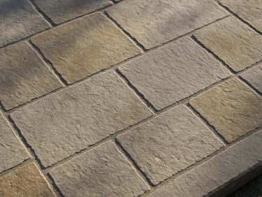 Overhead close-up of a newly laid stone patio, tight mortar joints and clean edging, daylight casting low shadows across the surface texture