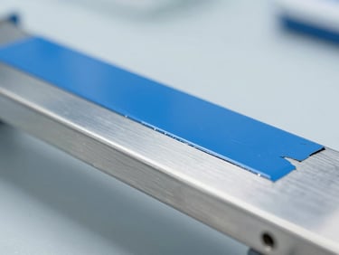 Macro shot of a clean metal surface half-stripped of blue paint, showing pristine steel underneath, clinical laboratory background, bright lighting, cool tones.