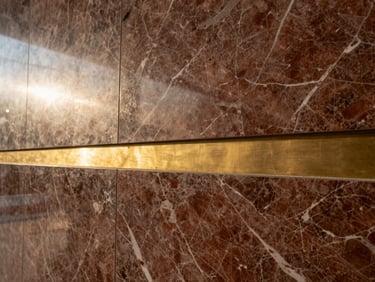Macro architectural detail of polished marble veining and brushed brass inlay on a premium feature wall.
