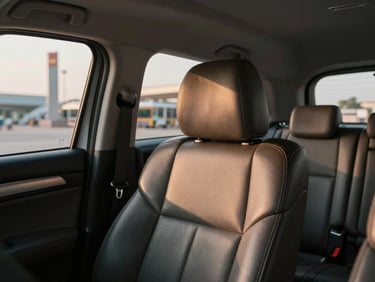 Close framing inside a clean private vehicle, leather seat and dashboard visible, Vientiane airport terminal glimpsed through windshield, warm afternoon light through glass