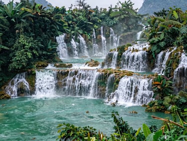Environmental wide-shot of Kuang Si waterfall tiered pools in dappled jungle light, turquoise water visible through green foliage, morning mist, no tourists in frame