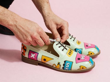 Hands carefully polishing a vintage-style shoe with colorful graphic prints, warm direct studio lighting, 35mm