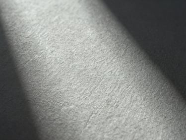 Macro close-up of heavy linen paper texture with subtle blind debossing, cool single-source light from the side, deep elegant shadows.