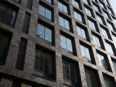 Low-angle architectural perspective of a modern dark stone and glass office building facade, sharp geometric shadows.
