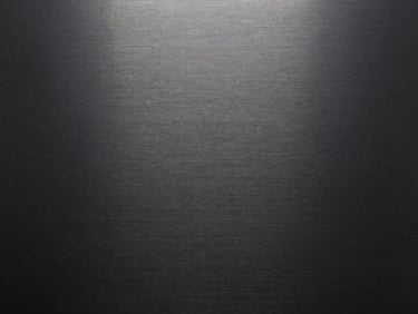 Macro texture of dark brushed metal with clean horizontal grain, high-contrast overcast lighting.