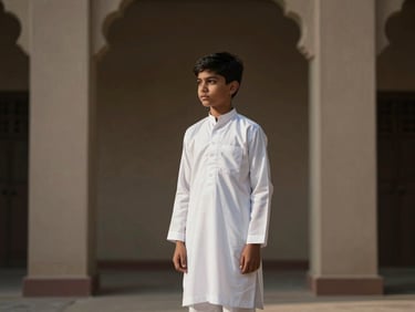 Young boy in a structured white shalwar kameez, standing in a minimalist architectural setting, cinematic natural light.