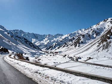 Panoramic view of a Himachal Pradesh mountain valley with a road visible in the foreground, vehicle tracks in snow, clear blue sky, midday light