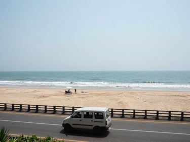 Wide panoramic view of Puri beach coastline in Odisha at midday, a road vehicle on the coastal highway in the foreground, documentary framing with natural overhead light