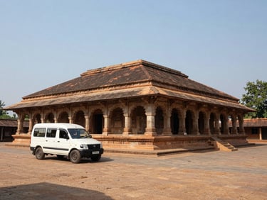 Wide shot of a Karnataka heritage site exterior at midday, a vehicle parked outside, documentary travel style, clear sky