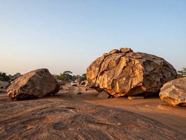 Wide shot of Hampi boulder landscape at golden hour, a road vehicle visible on a dirt track in the middle distance, documentary framing, operational travel context