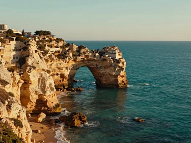 Cinematic shot of the Algarve coastline with dramatic limestone cliffs and turquoise sea arches under golden-hour sunlight.
